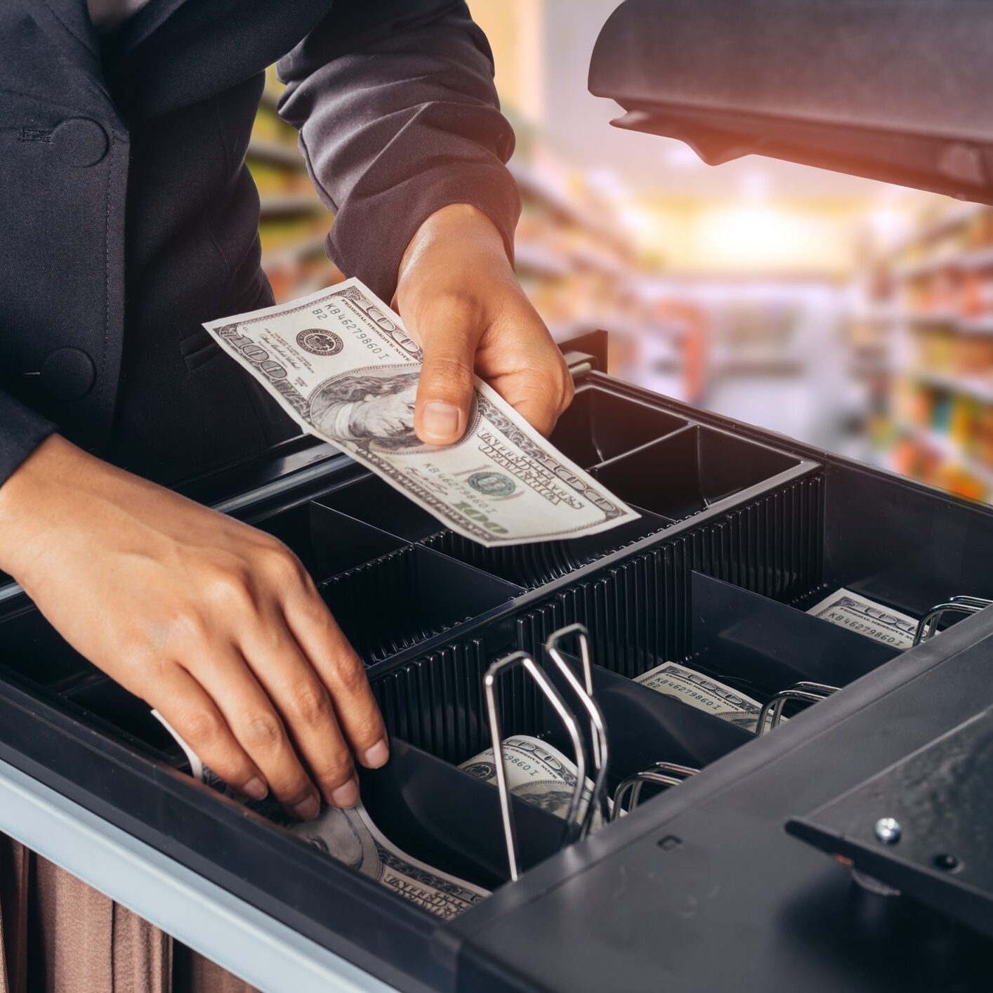 Person handling cash at a register drawer.